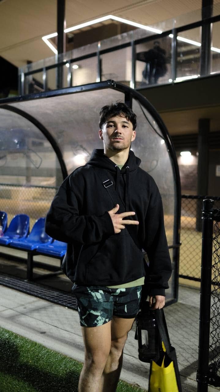 Player in a black hoodie standing in front of the dugout