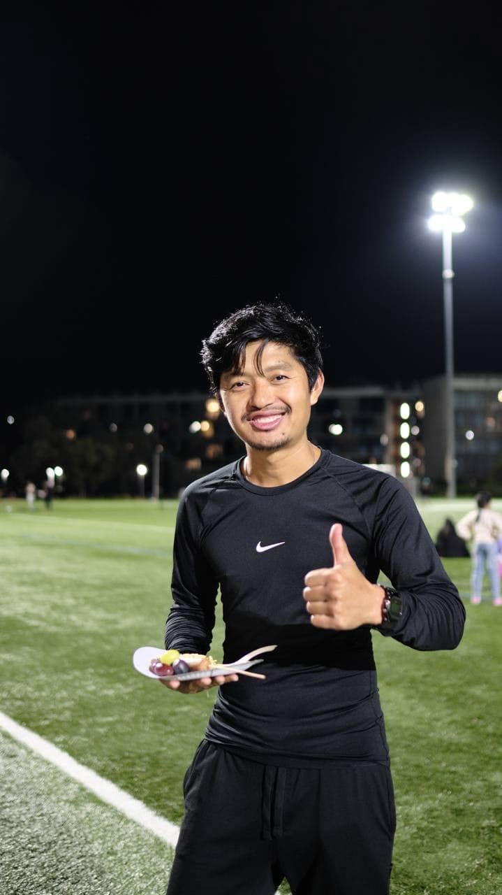 Smiling player in black giving a thumbs up under the floodlights