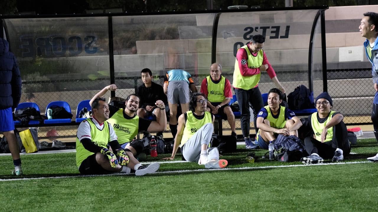 Players in yellow-green bibs resting on the turf by the bench
