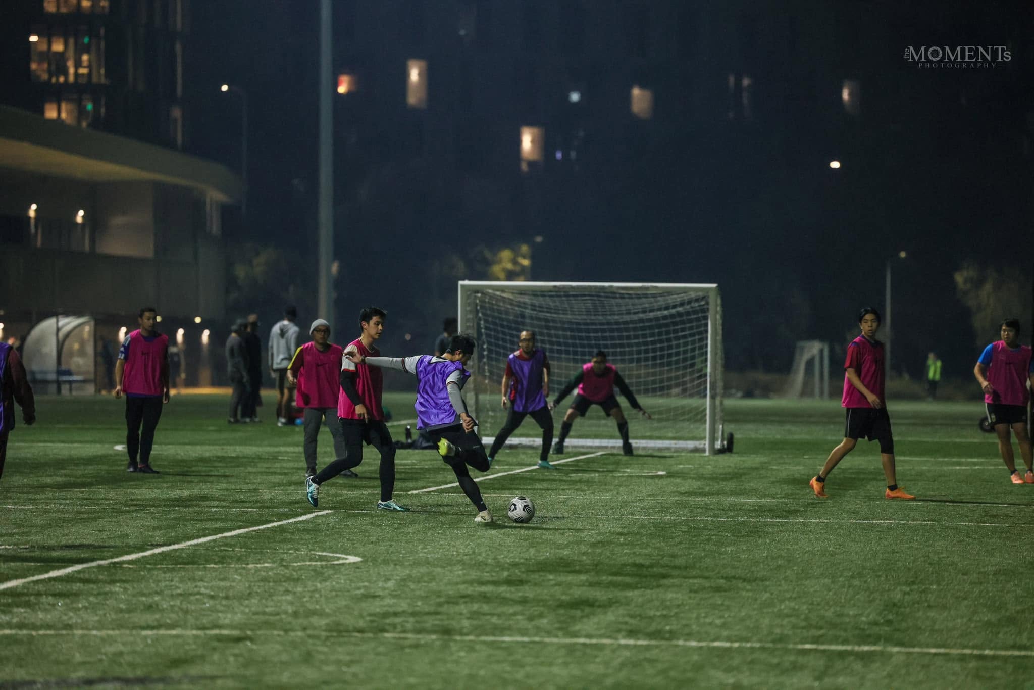 A player in a purple bib striking the ball with the goalkeeper set