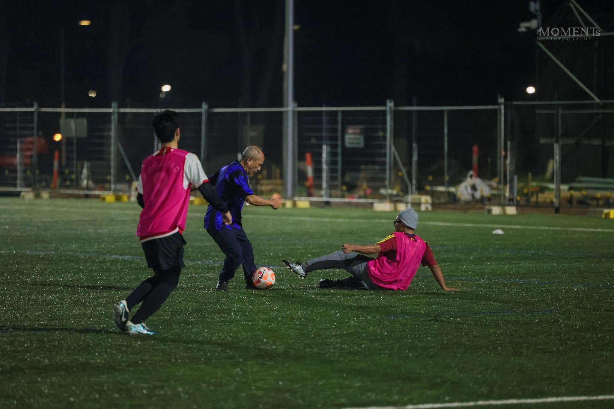 An older player in a blue shirt shielding the ball from a sliding challenge
