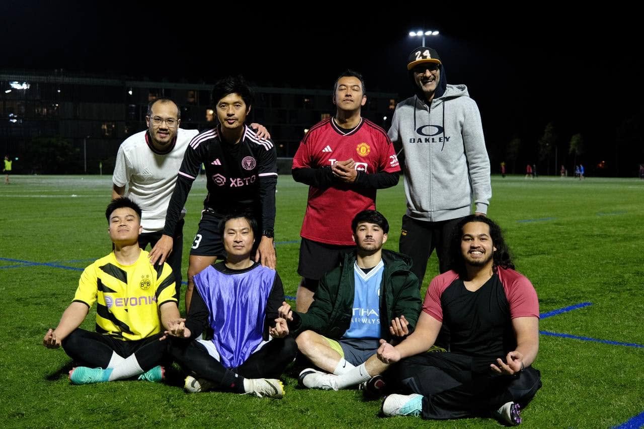 Seven players sitting cross-legged in a meditation pose on the pitch