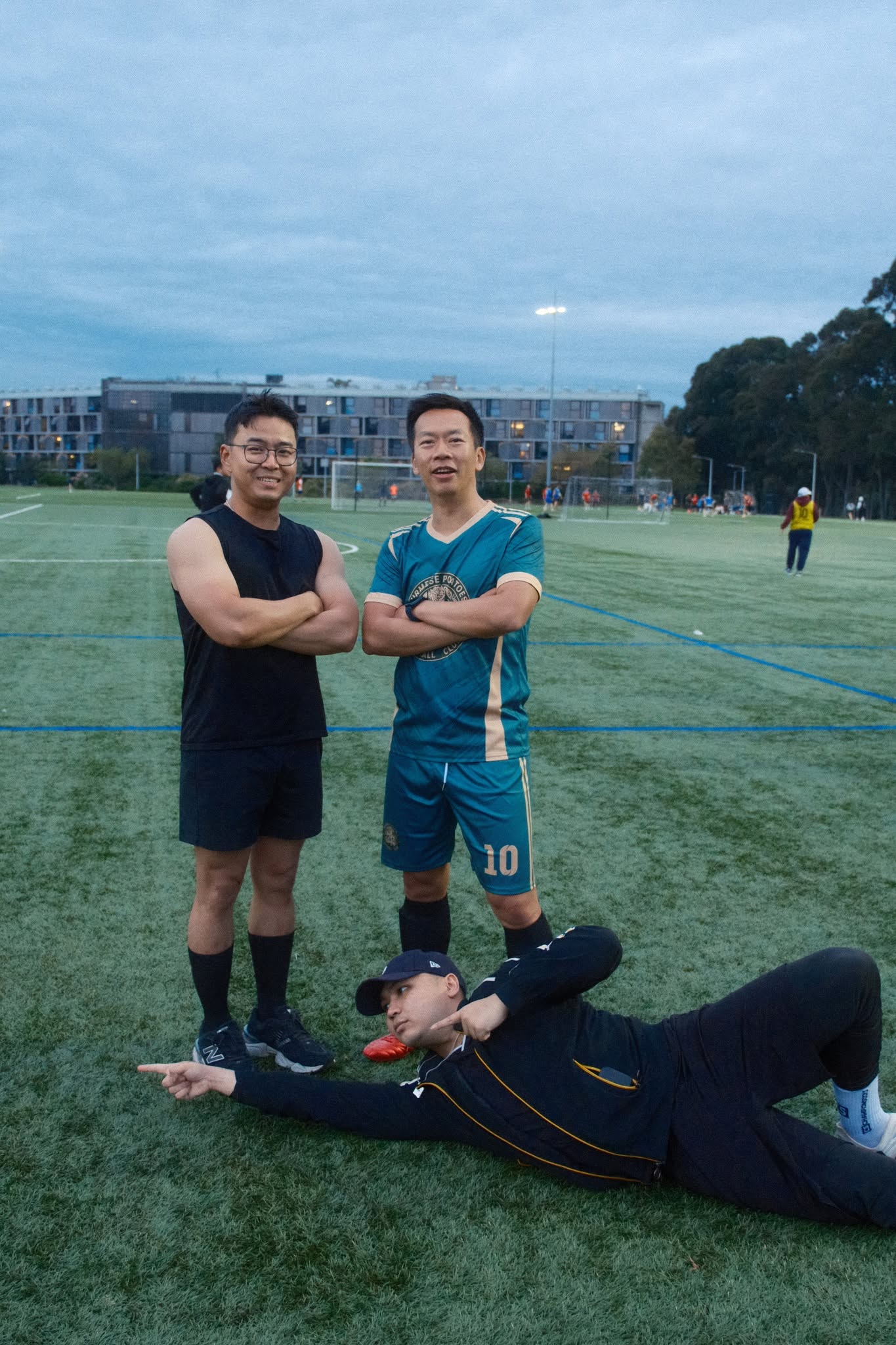 Two players standing with arms crossed and one lying on the grass