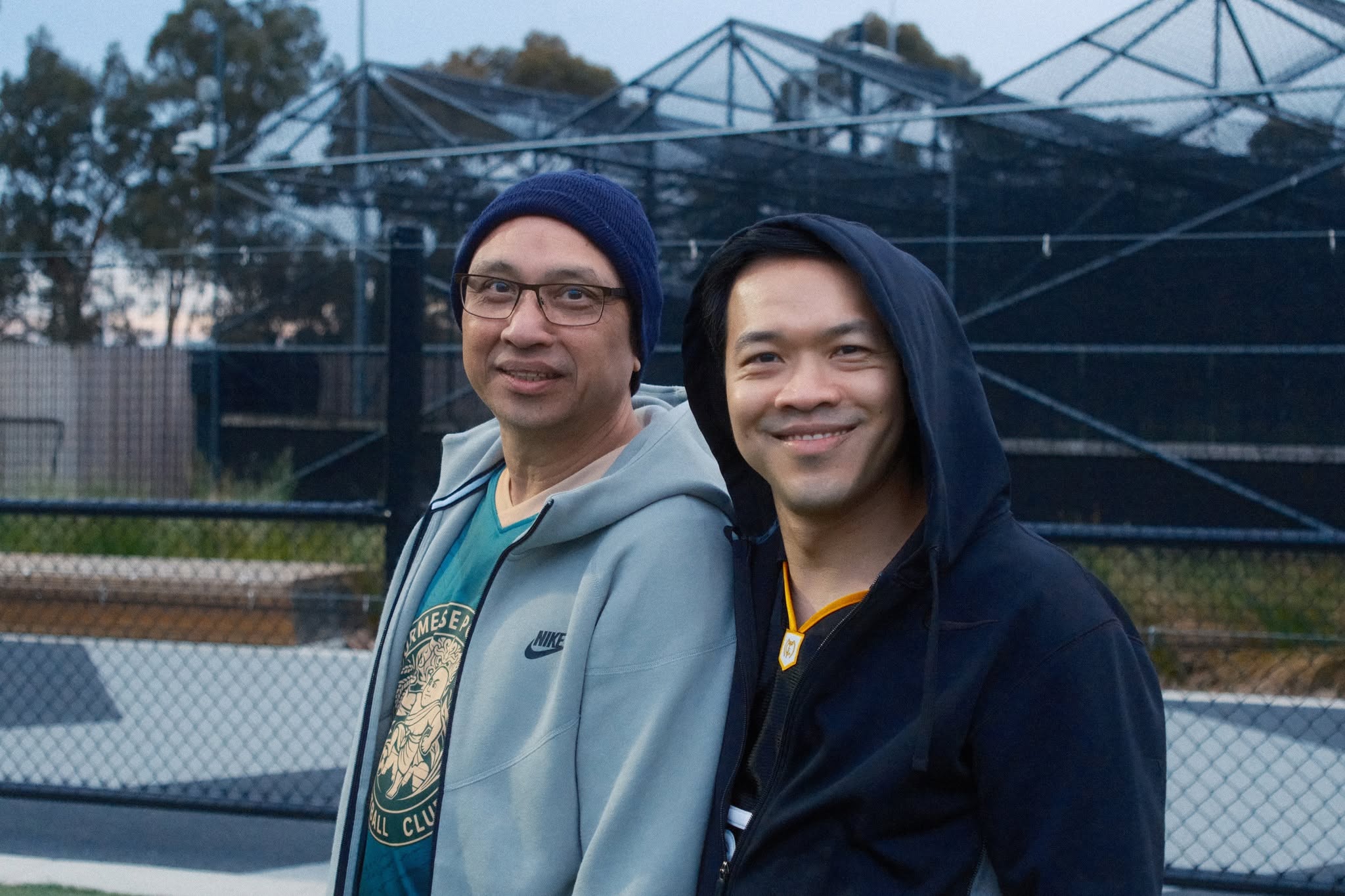 Two friends smiling beside the pitch fence