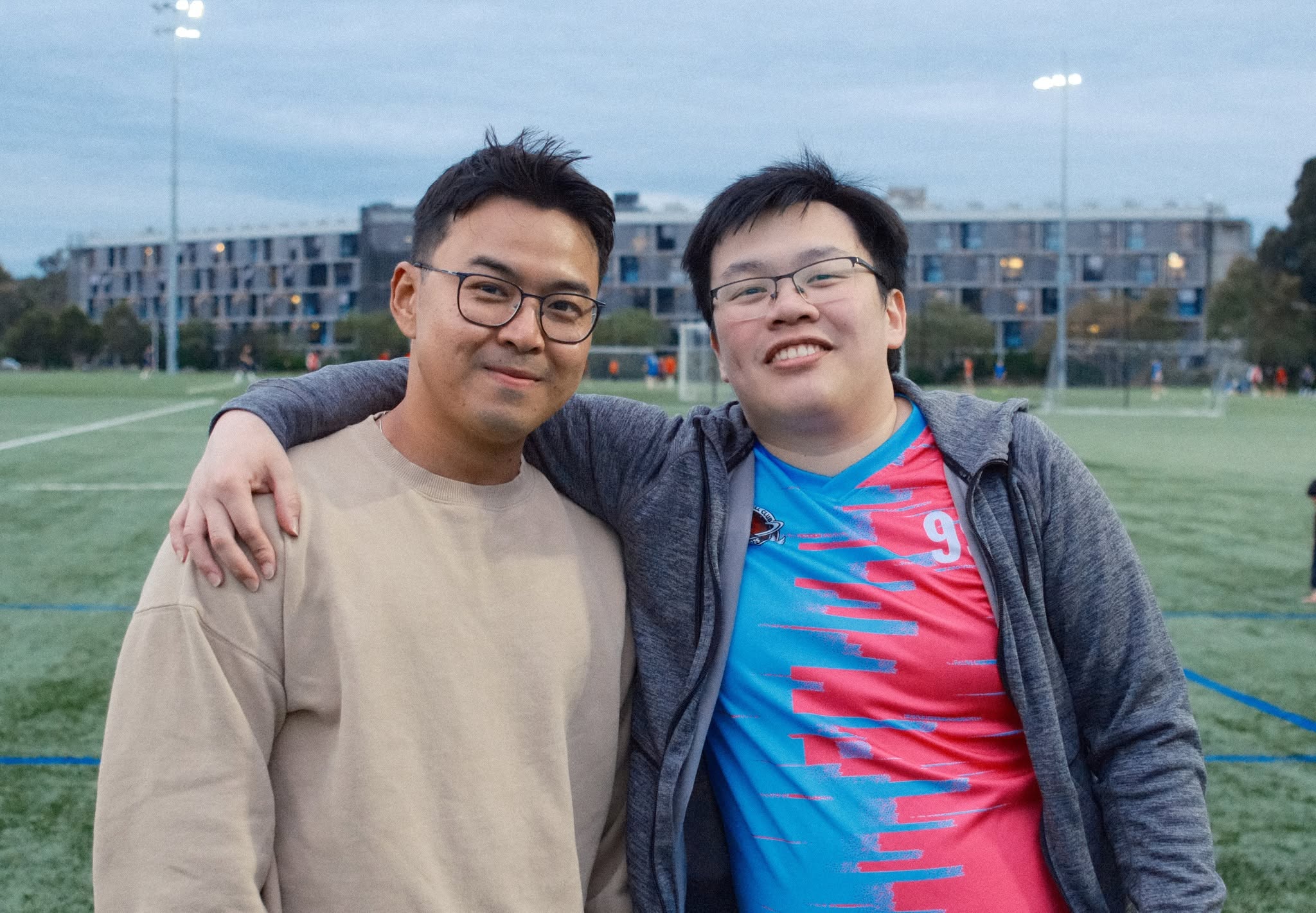 Two friends with arms around each other, one in a pink and blue shirt