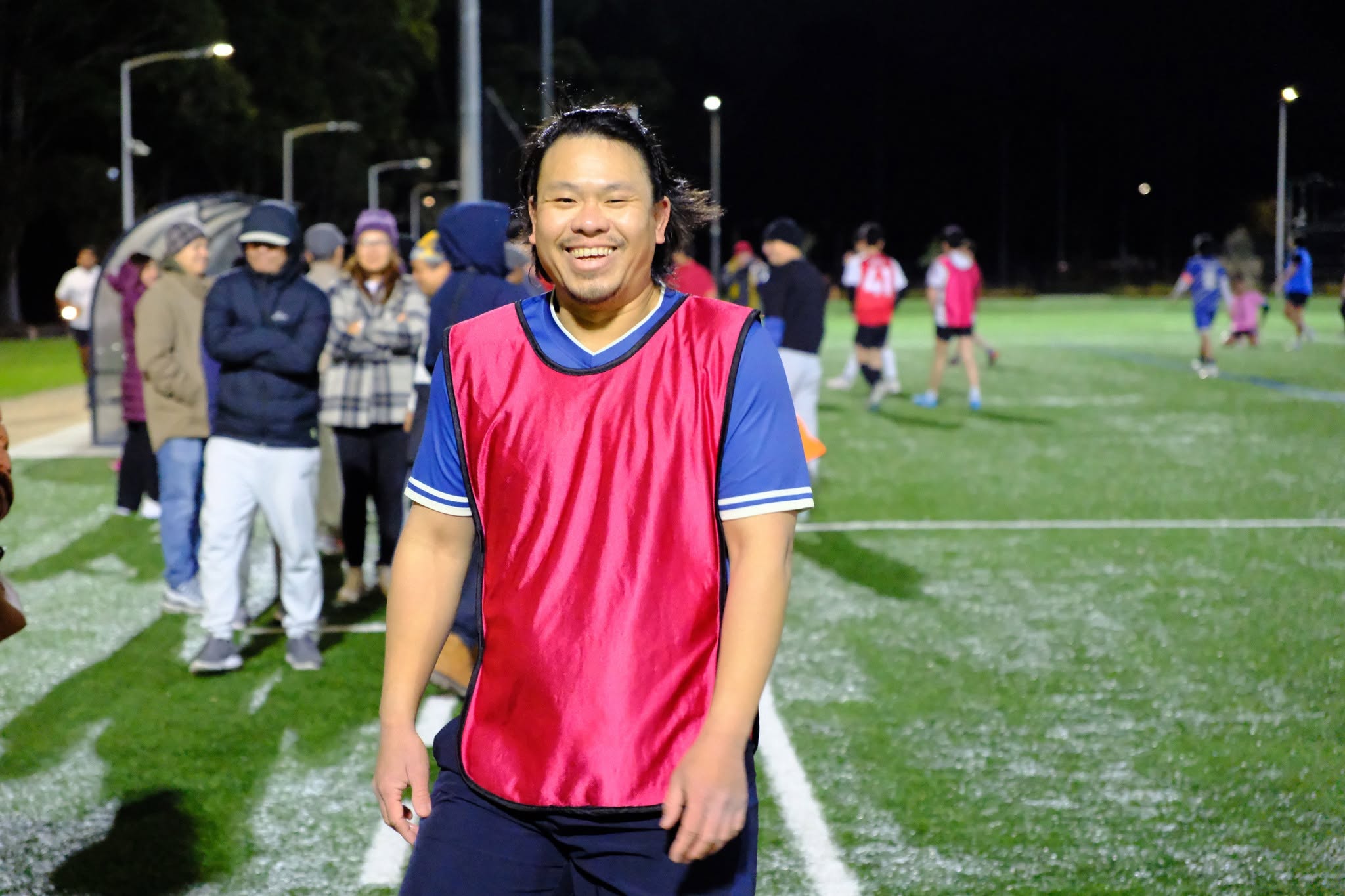 Smiling player in a red bib with the night game behind