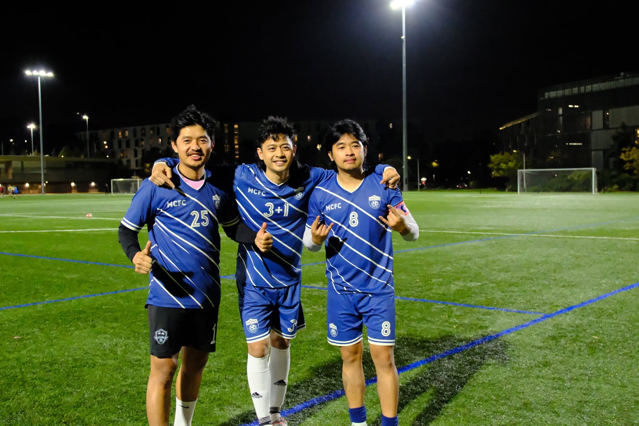 Three players in blue shirts posing arm in arm under the lights