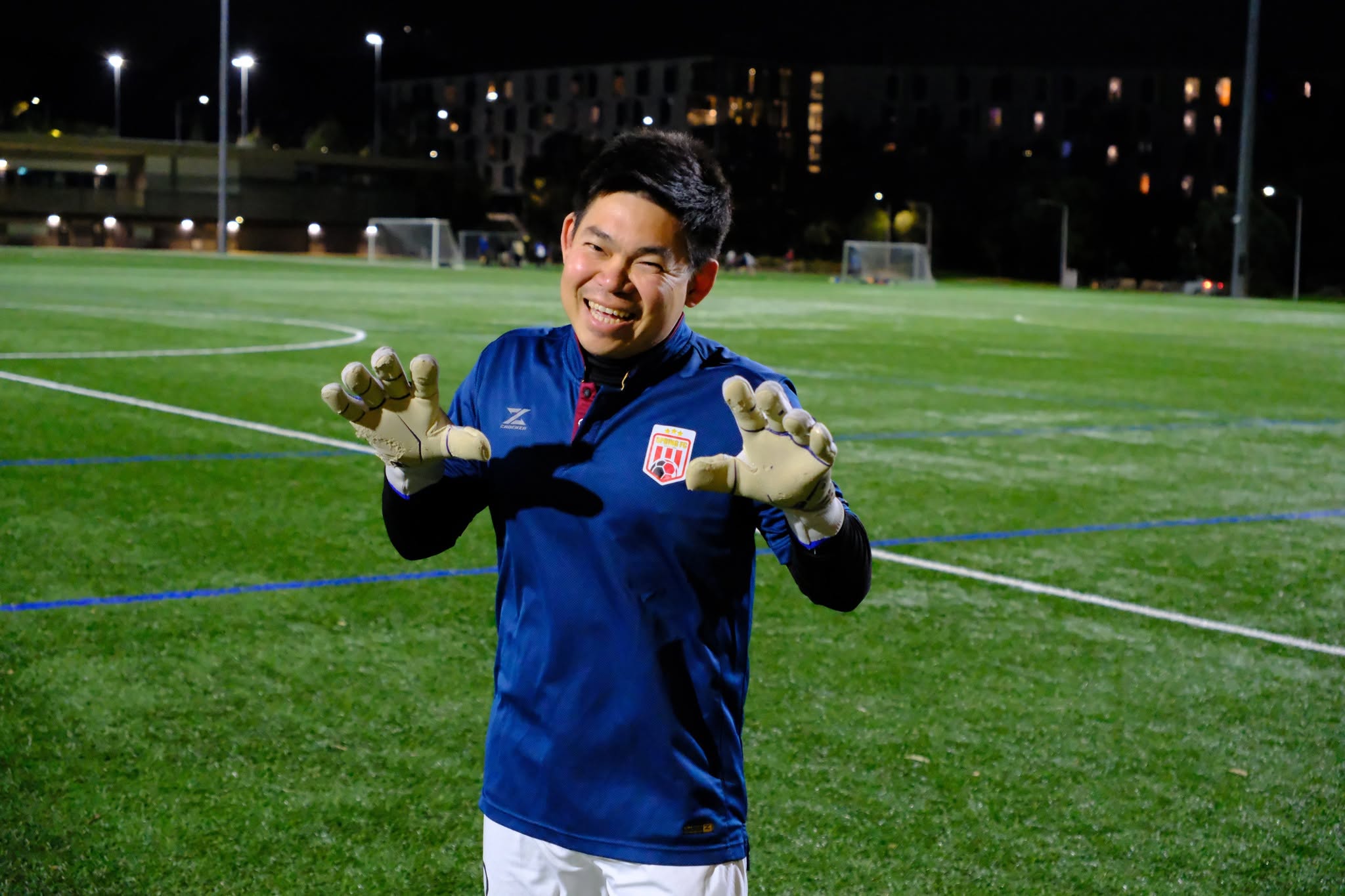Goalkeeper in a navy shirt holding up his gloves and smiling