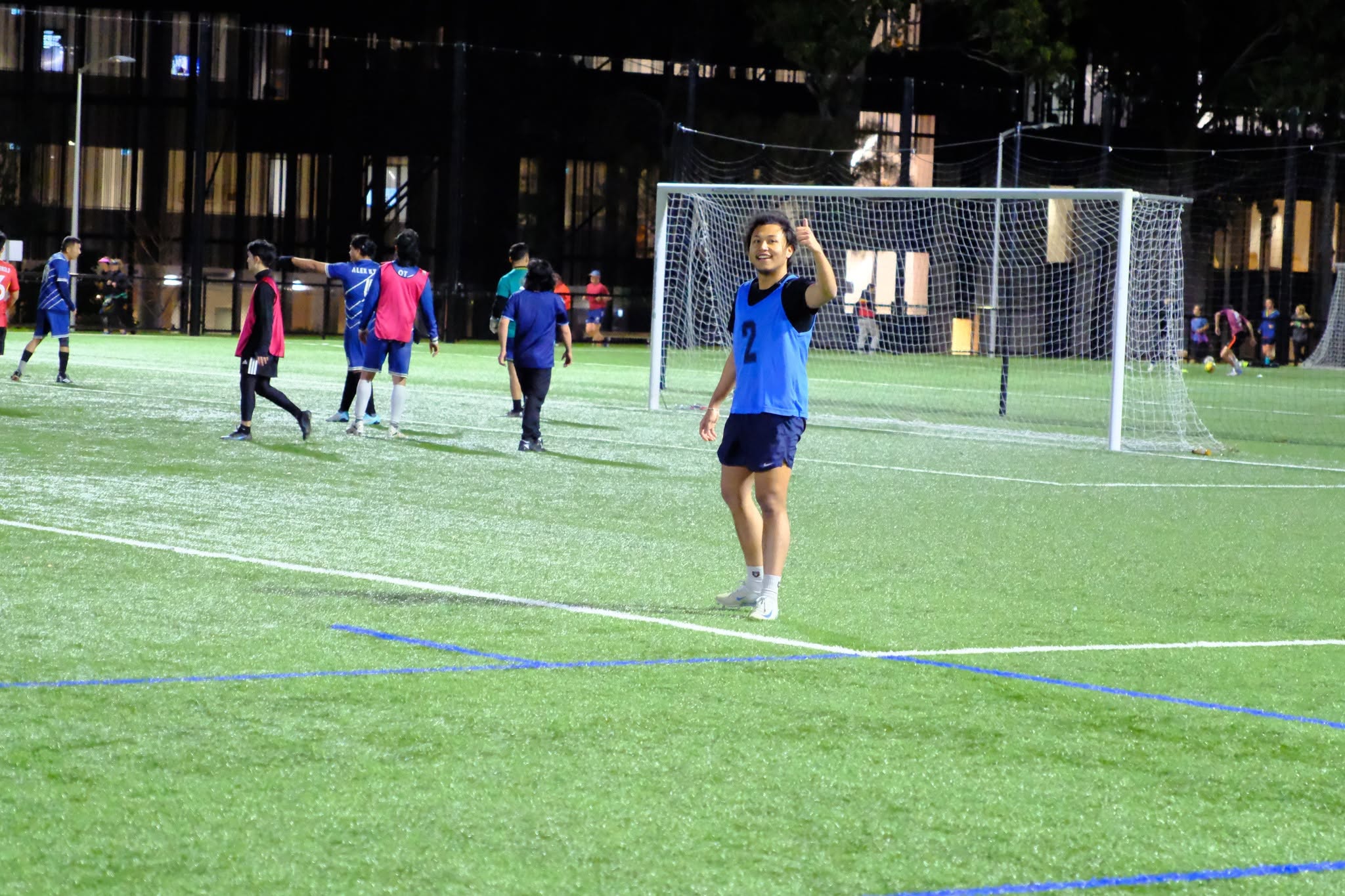 Player in a blue bib standing in front of the goal at night