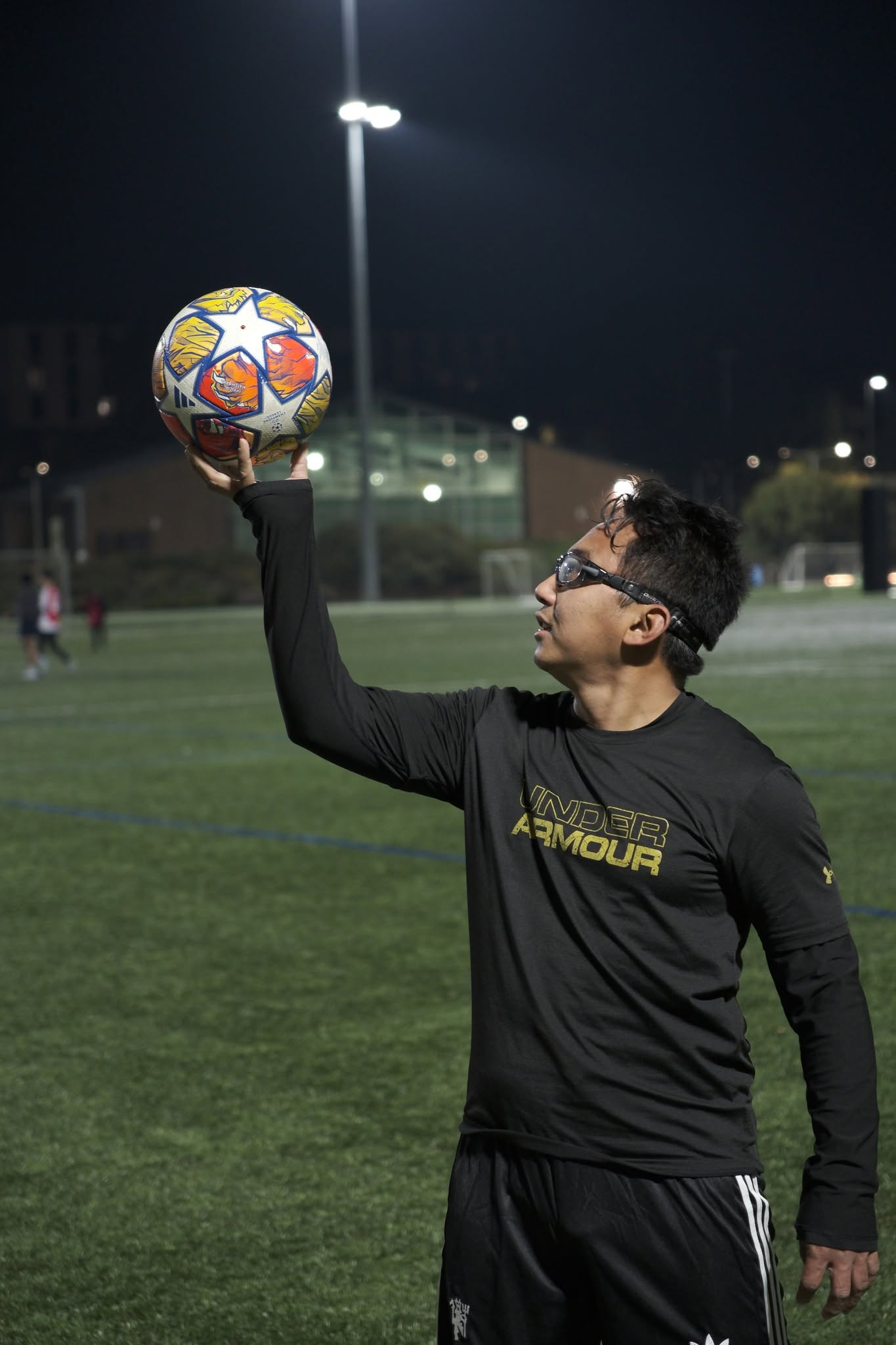 Player in black holding a ball up in one hand under the floodlights
