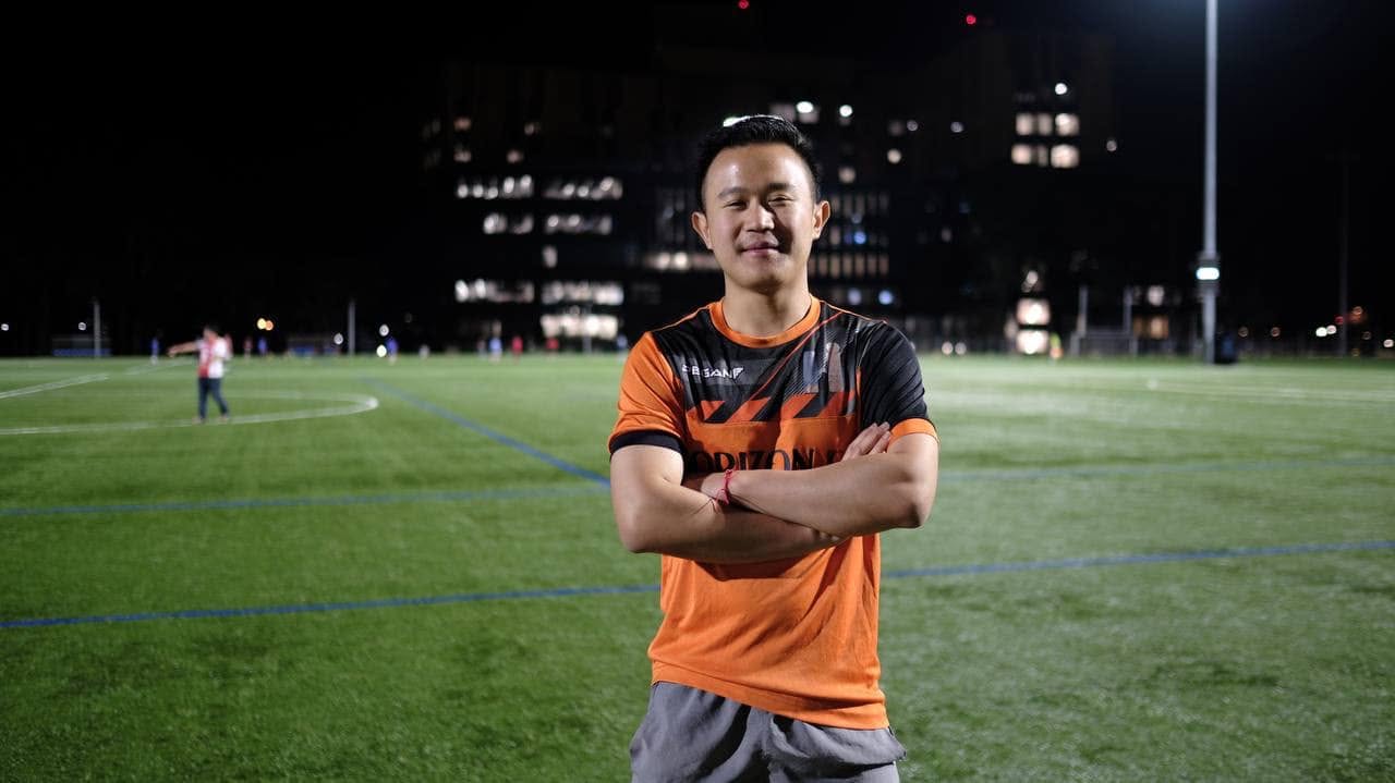 Player in an orange shirt with arms crossed on the pitch at night